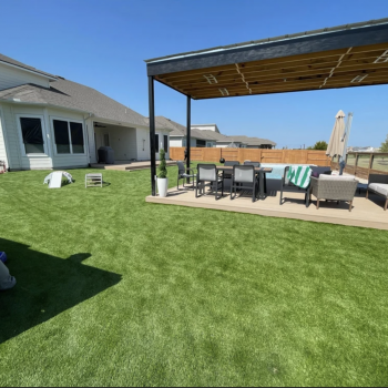 A wide shot of a backyard with artificial turf installed around a pergola with seating in the middle.